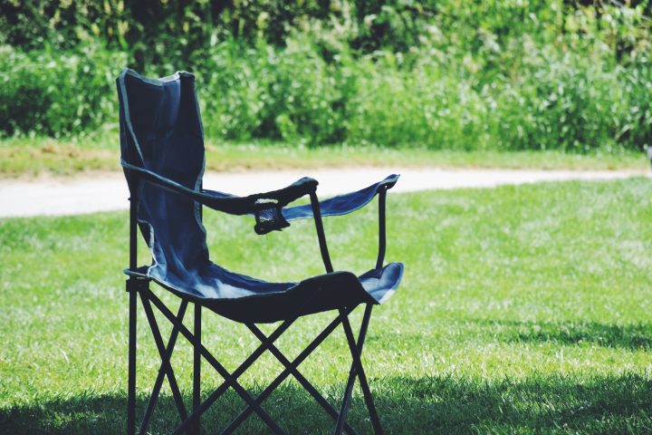 An empty lonely camping foldable lawn chair standing in a shade under a tree