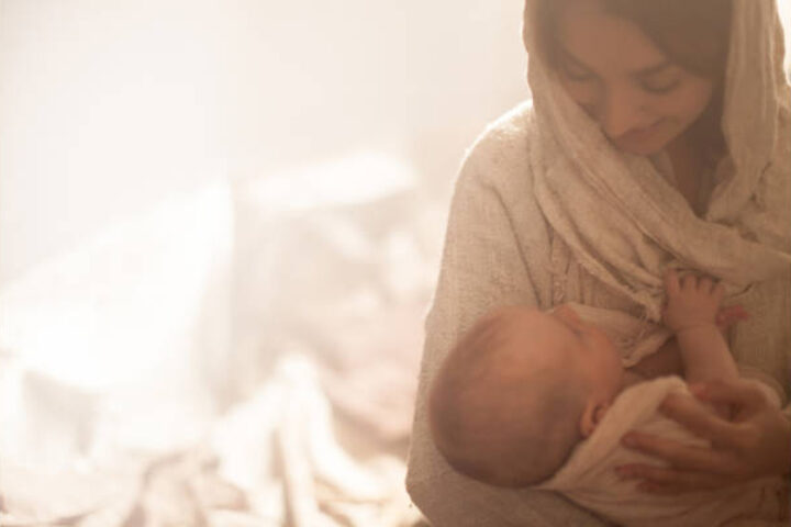 Warm-toned image of a mother cradling her newborn baby in her arms, looking down with care.