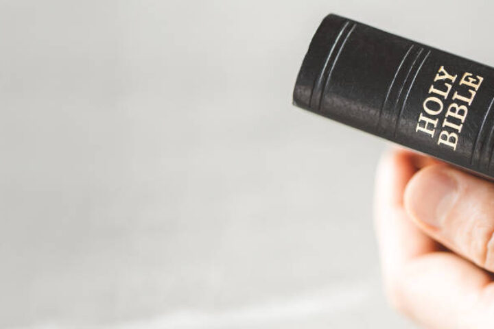 A person holds a small black Holy Bible with white lettering visible on the spine.