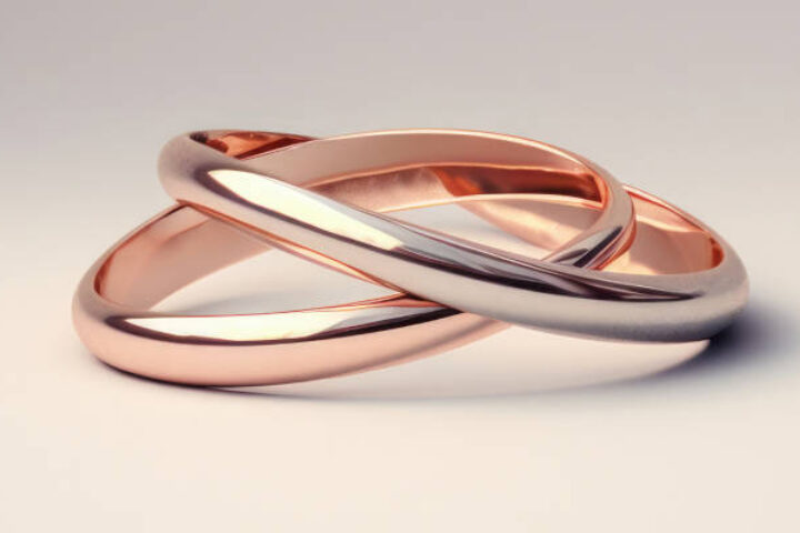 Two intertwined wedding rings, one rose gold and one white gold, on a pale gradient background.